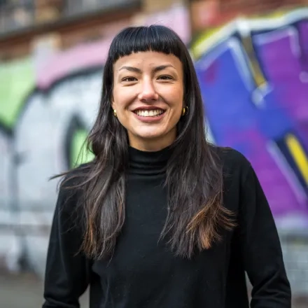 Foto Joy Hwang (lachende Person vor einer Wand mit Graffiti)